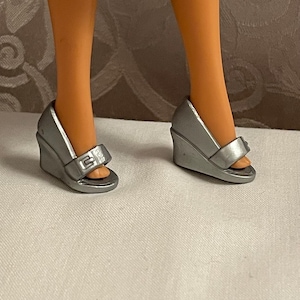 May include: Silver wedge sandals with a buckle detail. The sandals have a peep-toe design and a wedge heel. The shoes are made of a shiny, metallic material.