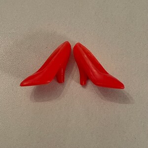 May include: A pair of red high-heeled shoes. The shoes are made of plastic and have a pointed toe.