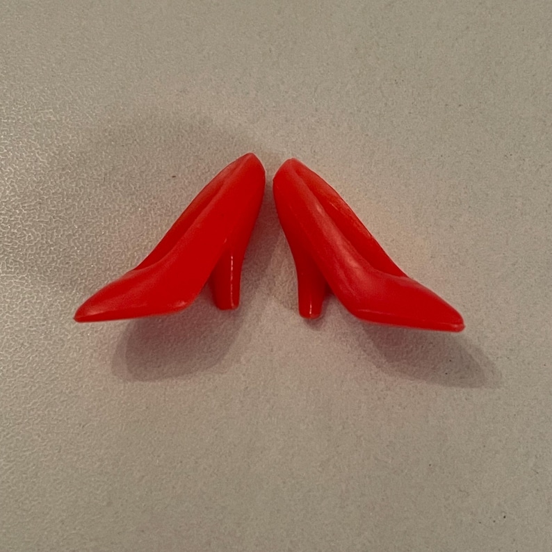 May include: A pair of red high-heeled shoes. The shoes are made of plastic and have a pointed toe.