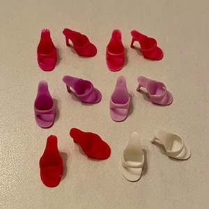 May include: A collection of ten pairs of doll shoes in pink, red, and white. The shoes are all different styles, including sandals, pumps, and flats.