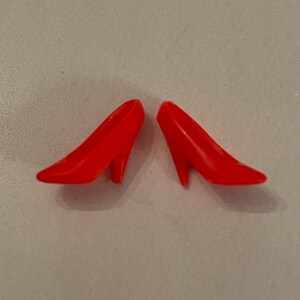 May include: A pair of bright red high-heeled shoes made of plastic. The shoes are pointed-toe and have a simple design.