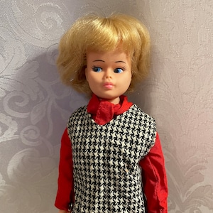 May include: A vintage doll with blonde hair, blue eyes, and a red and black houndstooth dress.