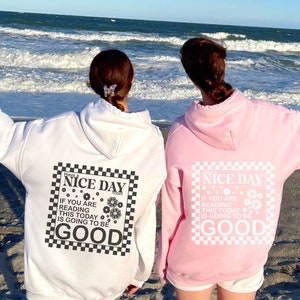 May include: Two people wearing white and pink hoodies with a black and white chequered graphic that says "Have a Nice Day Today" and "If you are reading this today is going to be good".