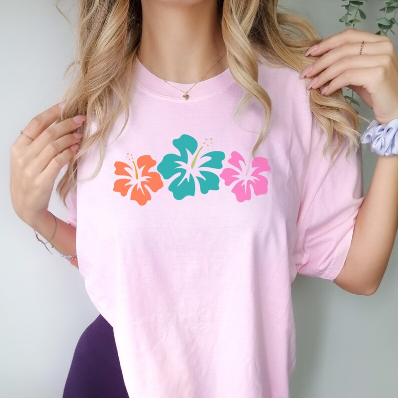 May include: A pink t-shirt with a row of three hibiscus flowers in orange, teal, and pink.