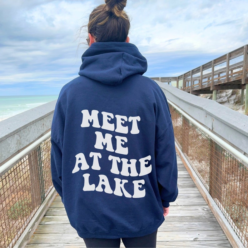 May include: A navy blue hooded sweatshirt with the text "MEET ME AT THE LAKE" in white retro-style lettering on the back.