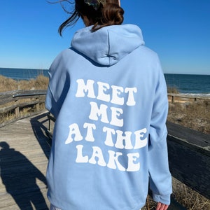 May include: A light blue hoodie with a white graphic that says "Meet Me At The Lake" in a retro font.