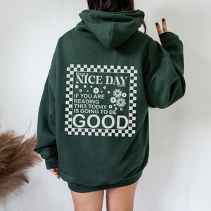 May include: A dark green hooded sweatshirt with a white graphic print on the back. The graphic features a checkered border and the text "Have a NICE DAY TODAY IF YOU ARE READING THIS TODAY IS GOING TO BE GOOD".