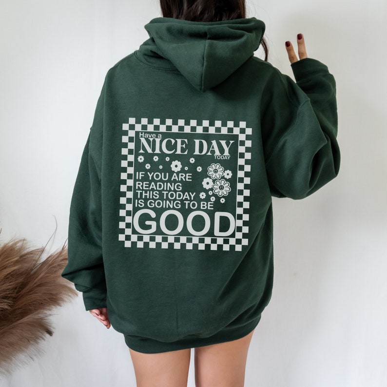 May include: A dark green hooded sweatshirt with a white graphic print on the back. The graphic features a checkered border and the text "Have a NICE DAY TODAY IF YOU ARE READING THIS TODAY IS GOING TO BE GOOD".