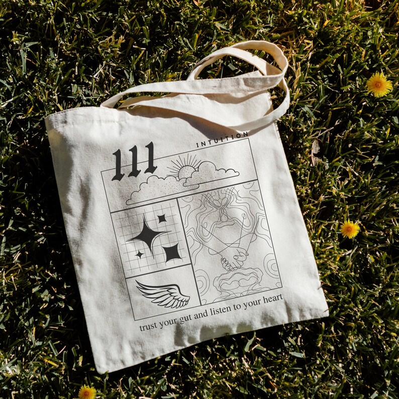 K&ouml;nnte beinhalten: Eine wei&szlig;e Tragetasche mit schwarzem Text und Grafiken. Die Tasche zeigt die Zahl 111, eine Sonne, Wolken, einen Stern, einen Fl&uuml;gel und den Text "INTUITION" und "vertraue deinem Bauchgef&uuml;hl und h&ouml;re auf dein Herz".