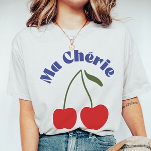 May include: White t-shirt with a blue graphic of two red cherries and the text "Ma Ch&eacute;rie".