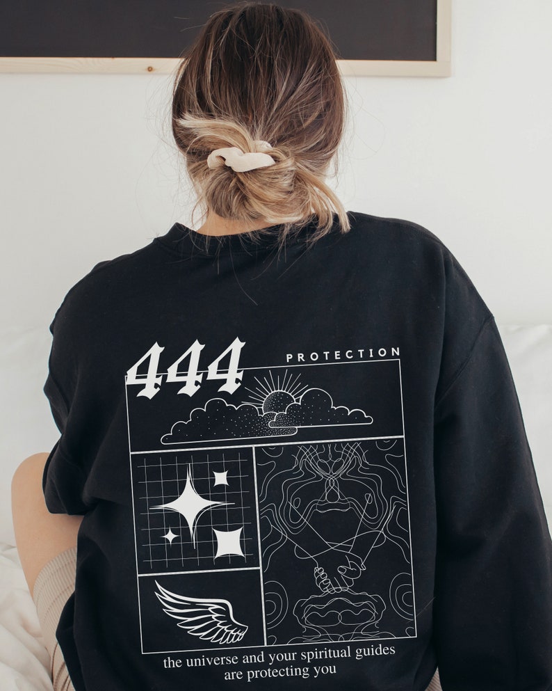 May include: Black sweatshirt with a white graphic design featuring the number 444, the words "Protection", a sun, clouds, stars, a wing, and two hands clasped together. The text below the graphic reads "the universe and your spiritual guides are protecting you".