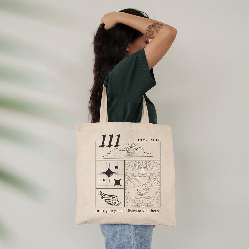 K&ouml;nnte beinhalten: Eine beige Tragetasche mit schwarzem Text und Illustrationen. Die Tasche zeigt die Zahl 111, das Wort "INTUITION", eine Sonne, Wolken, Sterne, einen Fl&uuml;gel und den Text "vertraue deinem Bauchgef&uuml;hl und h&ouml;re auf dein Herz".