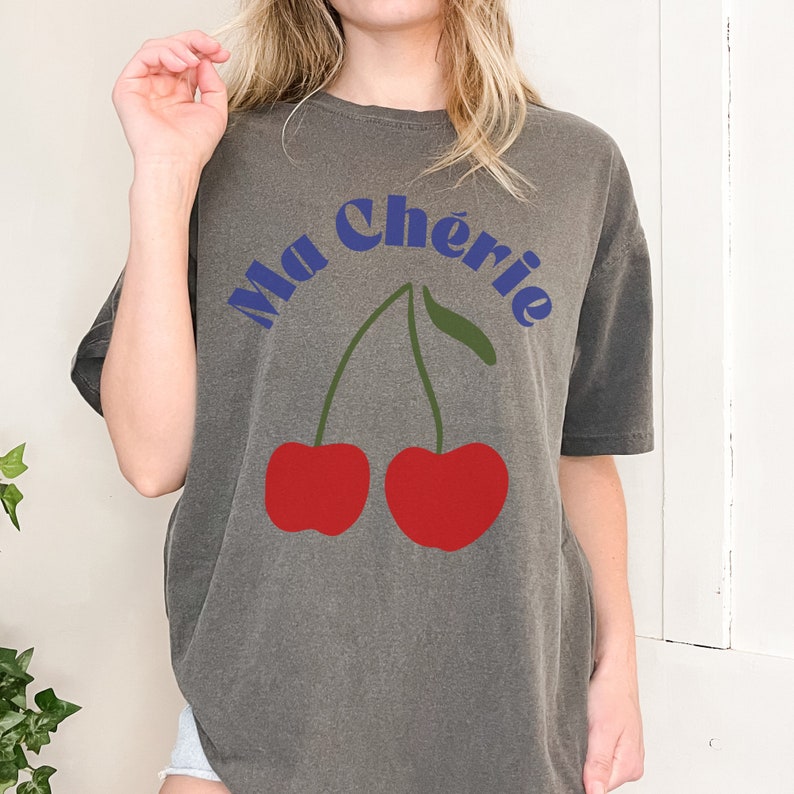 May include: A gray oversized t-shirt with a graphic of two red cherries and the text "Ma Ch&eacute;rie" in blue.