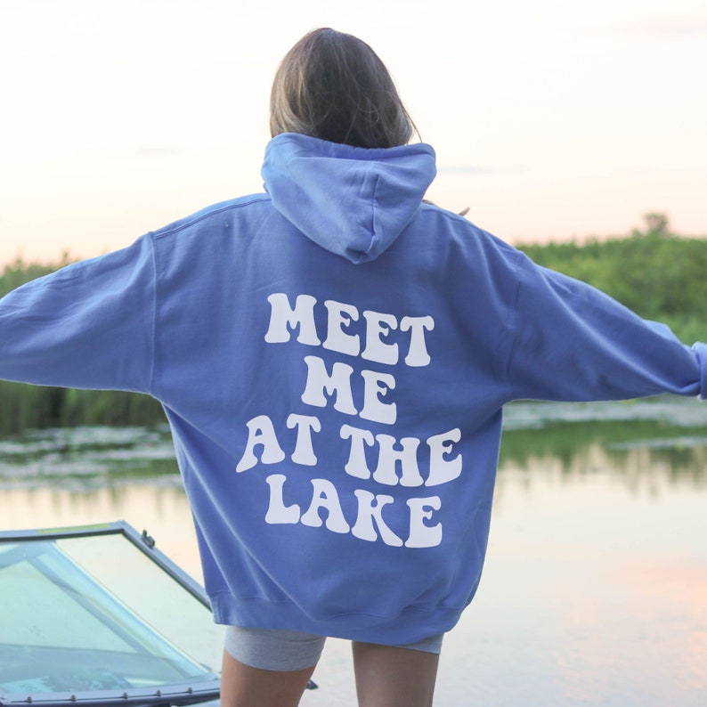 May include: A light blue hoodie with the text "MEET ME AT THE LAKE" in white retro-style lettering on the back.