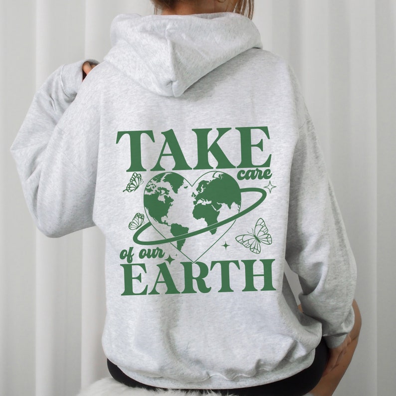 Op de afbeelding: Een grijze hoodie met een groene afbeelding op de rug. De afbeelding toont een hartvormige aarde met een ring eromheen, vlinders en de tekst "TAKE care of our EARTH".