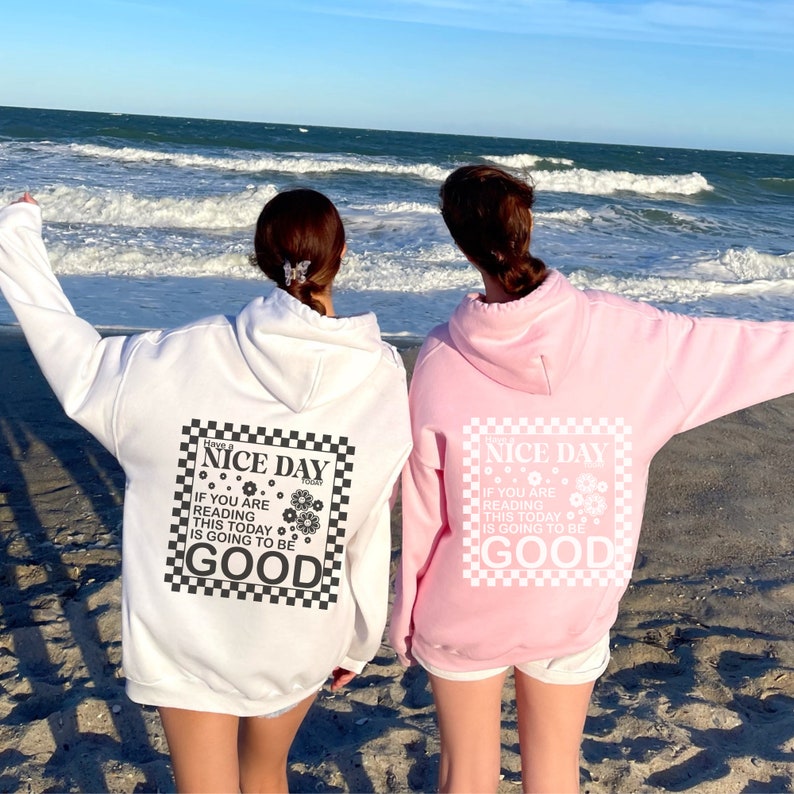 May include: Two people wearing white and pink hoodies with a black and white checkered graphic that says "Have a Nice Day Today" and "If you are reading this today is going to be good".