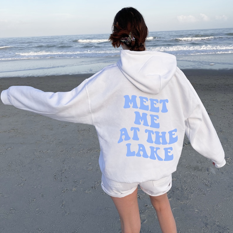 May include: White hoodie with a blue text graphic on the back that says "Meet Me At The Lake" in a retro font.