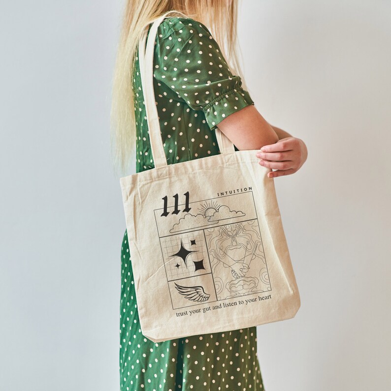 K&ouml;nnte beinhalten: Eine beige Tragetasche mit schwarzem Text und Illustrationen. Der Text lautet "111 Intuition vertraue deinem Bauchgef&uuml;hl und h&ouml;re auf dein Herz".