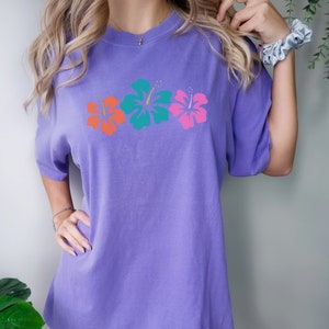May include: A purple oversized t-shirt with a graphic of three colorful hibiscus flowers.