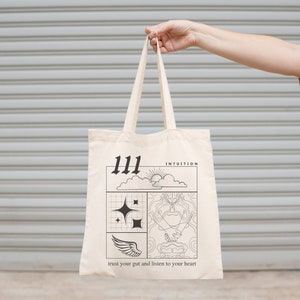 K&ouml;nnte beinhalten: Eine wei&szlig;e Canvas-Tragetasche mit schwarzem Text und Grafiken. Die Tasche zeigt die Zahl 111, das Wort "INTUITION" und den Spruch "vertraue deinem Bauchgef&uuml;hl und h&ouml;re auf dein Herz".