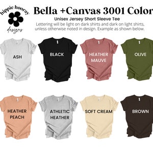 K&ouml;nnte beinhalten: Eine Auswahl an Bella + Canvas 3001 T-Shirts mit kurzen &Auml;rmeln in verschiedenen Farben, darunter Asche, Schwarz, Heidekraut-Mauve, Oliv, Heidekraut-Pfirsich, Athletik-Heidekraut, Weichcreme und Braun. Der Text "Lettering will be light on dark shirts and dark on light shirts, unless otherwise noted in design. Example as shown below." wird &uuml;ber den Shirts angezeigt.