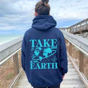 Op de afbeelding: Een marineblauwe hoodie met een turquoise print op de rug. De print toont een hartvormige aarde met vlinders en de tekst "TAKE care of our EARTH".