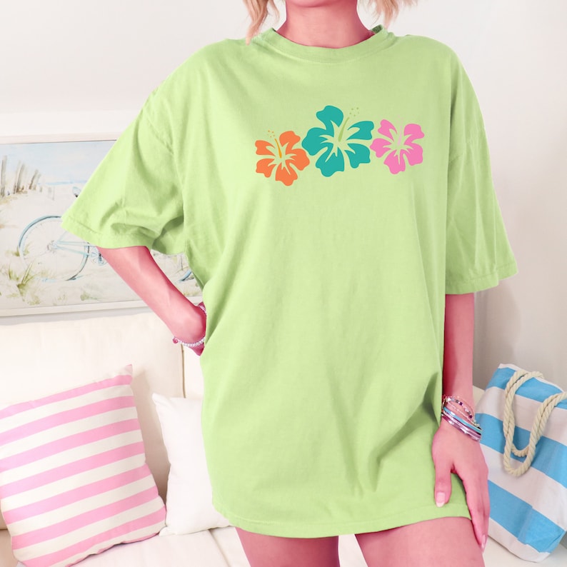 May include: A light green oversized t-shirt with a graphic of three tropical flowers in orange, teal, and pink.