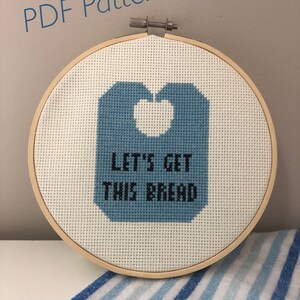 May include: A blue and white cross-stitch embroidery hoop with the text "Let's get this bread" in black lettering.