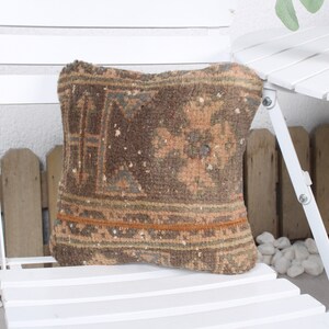 May include: A brown and beige patterned throw pillow with a brown fringe border. The pillow is sitting on a white wooden chair.