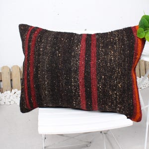 May include: A brown and red striped throw pillow with a textured woven fabric. The pillow is sitting on a white chair.
