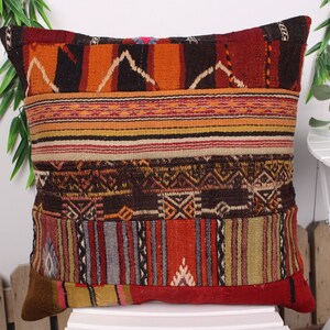 May include: Square decorative pillow with a patchwork design. The pillow features a mix of colors including red, orange, brown, and yellow. The pillow has a textured, woven appearance with geometric patterns.