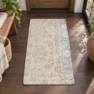 May include: A rectangular runner rug featuring a cream-colored base with a repeating floral pattern in shades of light blue and dark gray. The rug has a distinct vertical border on the right side with a dense blue and cream botanical design.