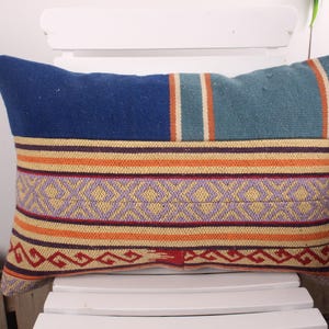 May include: Rectangular decorative pillow with a patchwork design. The pillow features a blue top, a teal section with orange stripes, and a patterned center with orange, purple, and yellow stripes. The bottom has a red and orange geometric pattern.
