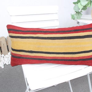 May include: A long, rectangular pillow with red, yellow, and black striped pattern. The pillow is made of woven fabric and is sitting on a white chair.