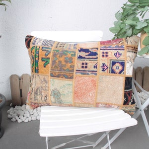 May include: Rectangular patchwork pillow with a variety of colors and patterns. The pillow is made of squares of fabric in shades of orange, blue, green, and beige. It is placed on a white chair outdoors.