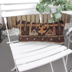 May include: A white folding chair with a patterned pillow. The pillow is brown, orange, and blue with a geometric design. The chair is made of metal and has a slatted seat.