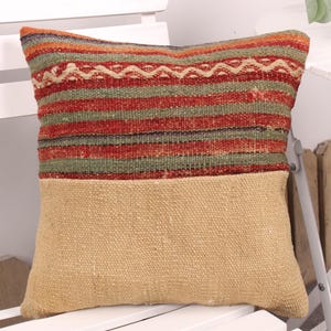 May include: A decorative pillow with a woven top section featuring horizontal stripes in red, green, and orange, with a cream-colored geometric pattern. The bottom half is a solid tan fabric. This pillow adds a touch of rustic charm to any room.