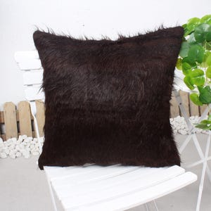 May include: A brown faux fur throw pillow with a soft, fluffy texture. The pillow is sitting on a white chair.