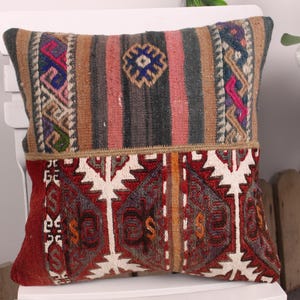 May include: A decorative pillow with a rectangular shape. The top section features vertical stripes in brown, pink, and gray, with a central geometric design. The bottom section has a red background with white and gray geometric patterns.