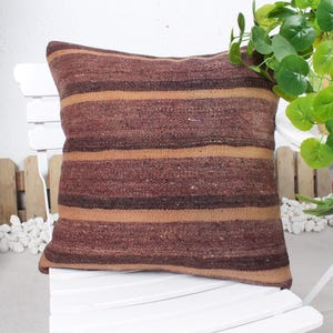 May include: A brown and beige striped throw pillow with a woven texture. The pillow is sitting on a white chair.