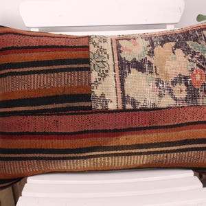 May include: Rectangular decorative pillow with a patchwork design. The pillow features a striped pattern in shades of red, orange, and black, with a floral pattern on one end. The pillow is placed on a white chair.