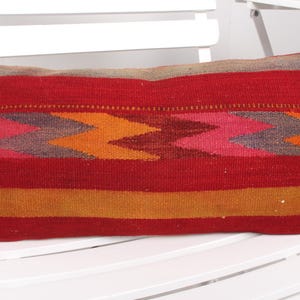 Puede incluir: Cojín de tiro rojo, naranja, rosa y gris con textura tejida. El cojín es rectangular y tiene un borde de flecos.