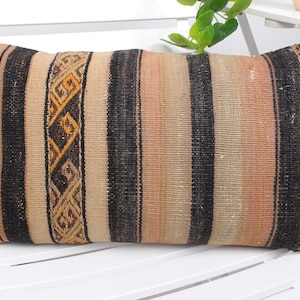 May include: A rectangular throw pillow with a striped pattern in shades of beige, brown, and black. The pillow has a woven texture and a geometric design on the edges.