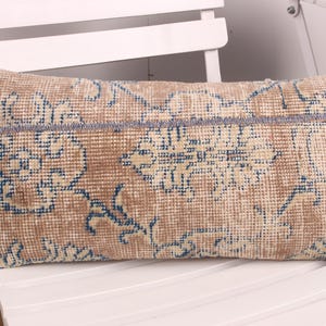 Peut inclure: Coussin rectangulaire beige avec un motif de tapis vintage. Le coussin présente un motif floral répété en bleu et crème. Le coussin est posé sur une chaise blanche.