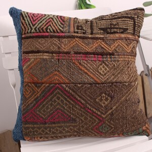 Könnte beinhalten: Ein dekoratives Kissen mit Patchwork-Design. Das Kissen zeigt geometrische Muster in Braun-, Orange-, Rosa- und Grüntönen. Die Kanten sind mit einem blauen Stoff verziert. Das Kissen liegt auf einem weißen Stuhl.