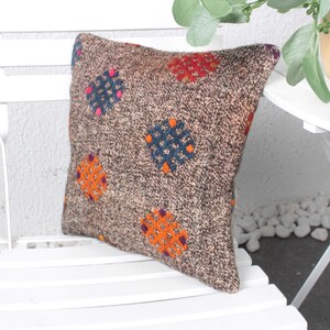 May include: A brown and beige throw pillow with a geometric pattern in shades of orange, blue, and purple. The pillow is sitting on a white wooden chair.
