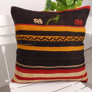 May include: A black, yellow, red, and cream striped throw pillow with geometric patterns. The pillow is made of woven fabric and has a fringed edge.