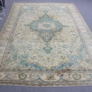 May include: Large rectangular rug with a central medallion design in shades of blue, beige, and green. The rug features an ornate border with floral and geometric patterns. The overall color palette is muted, creating a vintage or antique aesthetic.