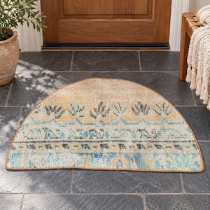 May include: A semi-circular area rug featuring a woven texture with a beige base color. The rug displays a repeating pattern of stylized dark gray floral motifs, horizontal blue zigzag lines, and a band of blue and gray geometric shapes.