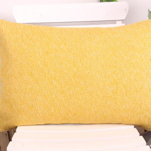 May include: A rectangular yellow decorative pillow with a textured surface. The pillow is resting on a white chair. The pillow's dimensions are approximately 20 inches long and 12 inches wide.